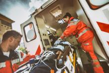 Two paramedics in orange uniforms and reflective vests loading a patient on a stretcher into an ambulance.